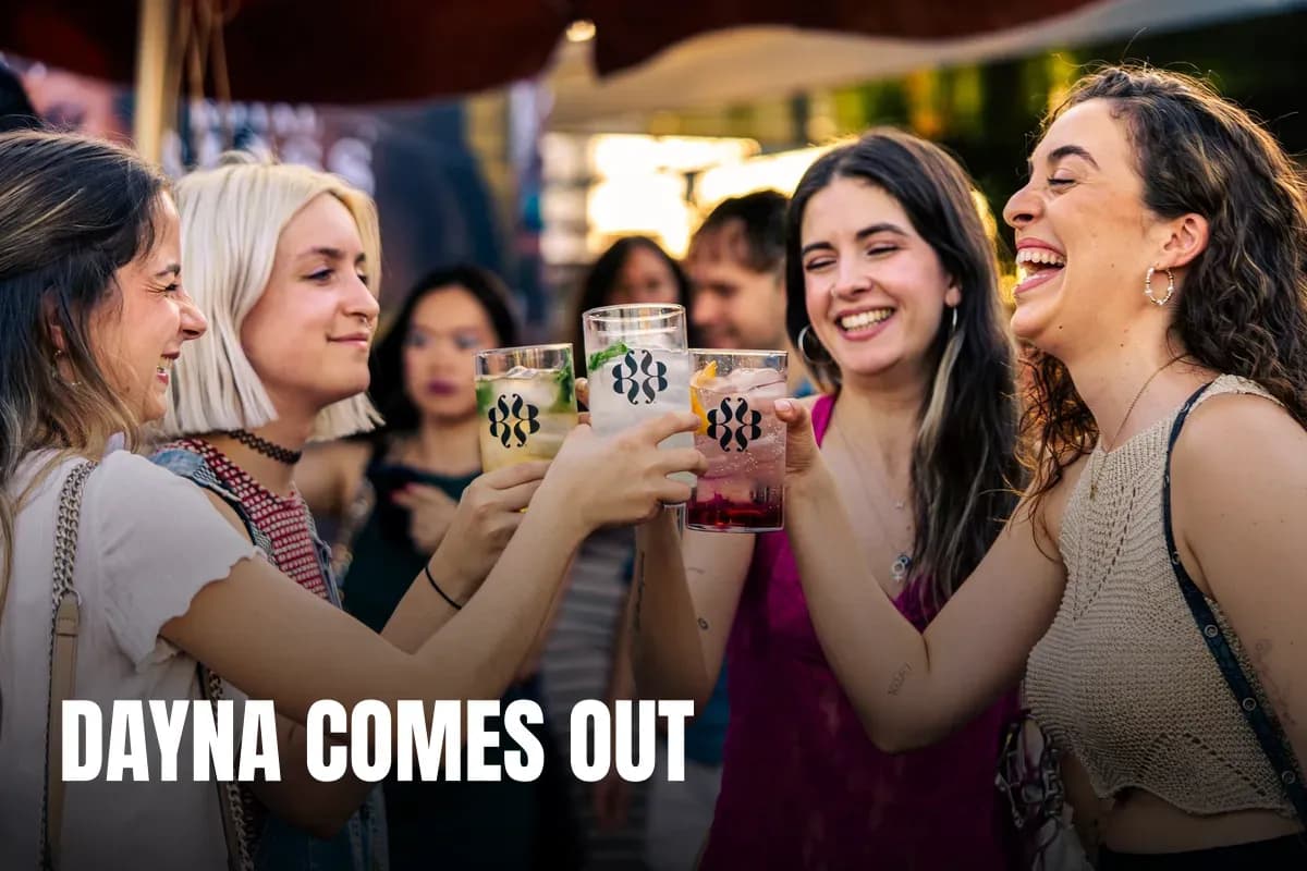 Young women laughing and clinking glasses in a lively outdoor setting, enjoying a festive atmosphere.