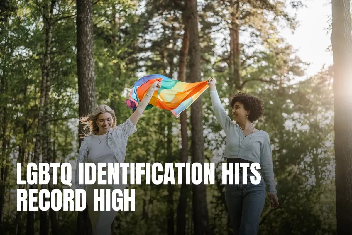 Two women joyfully holding a rainbow flag in a sunny forest setting, symbolizing LGBTQ pride.
