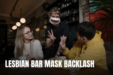 A woman and man use nonverbal gestures with a masked waitress in a cozy café.