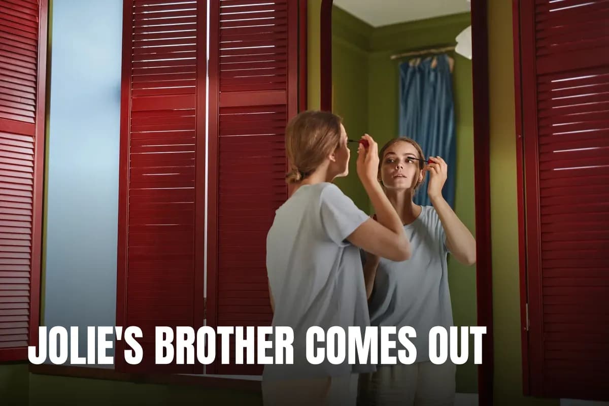 Woman applying mascara in front of a mirror with red shutters reflecting her image indoors.